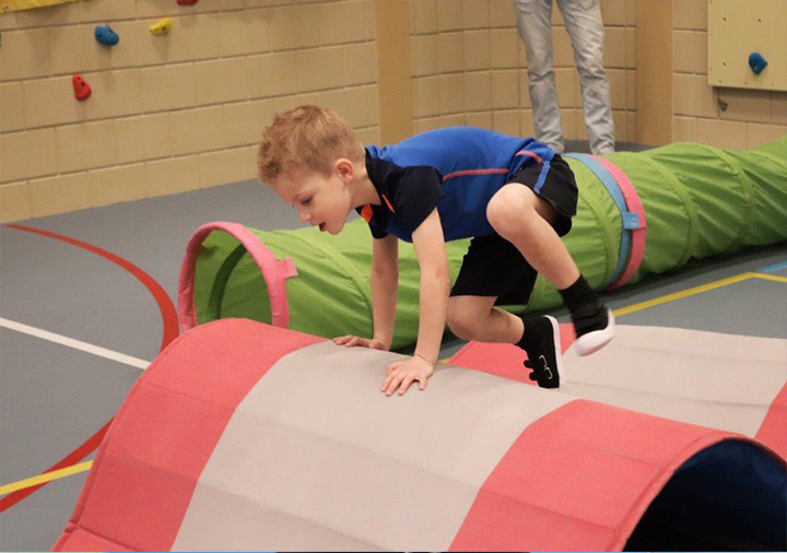 Jongen kruipt met een gordel om over een grote rol in de gymzaal