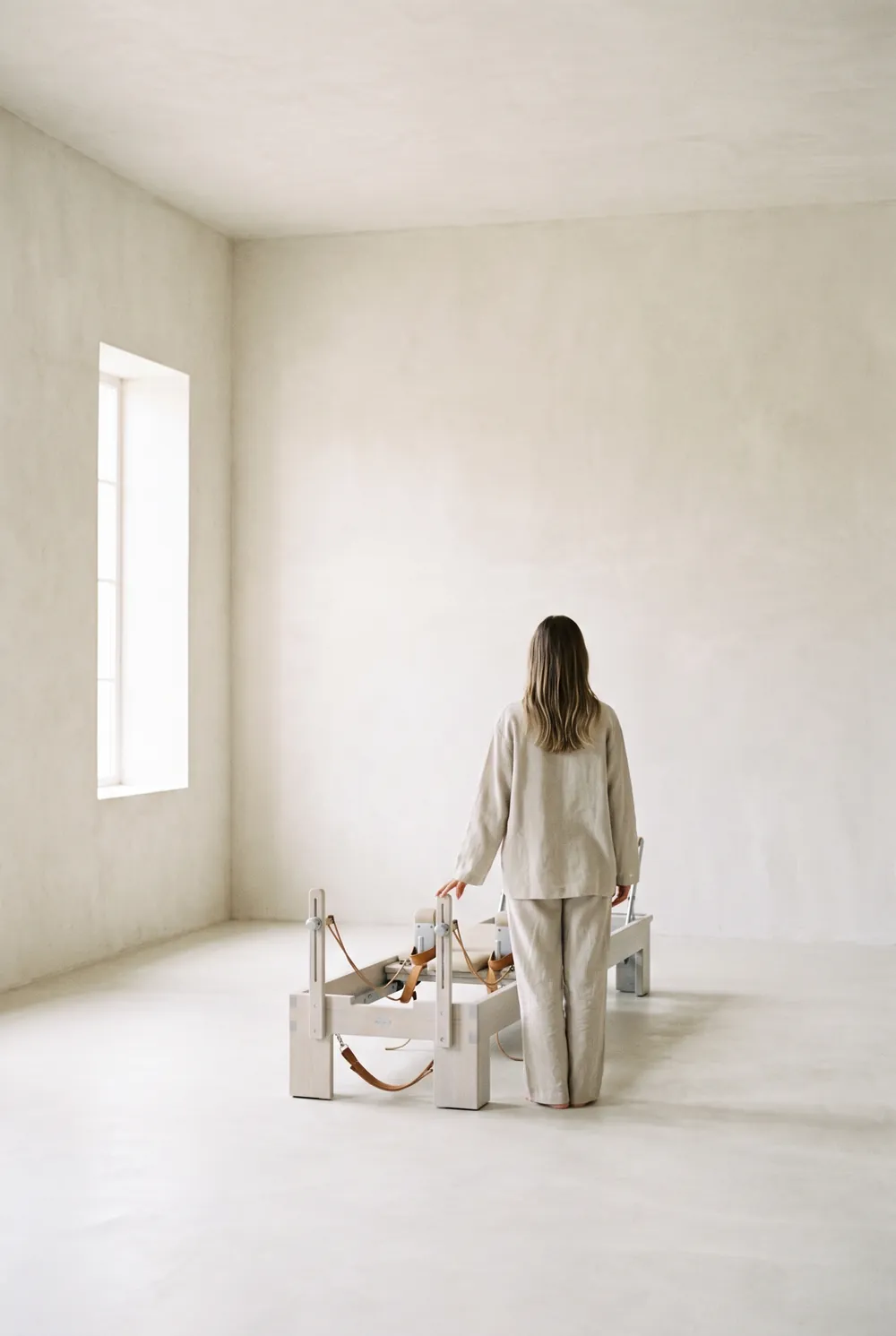 A woman standing beside a reformer in an empty plaster room