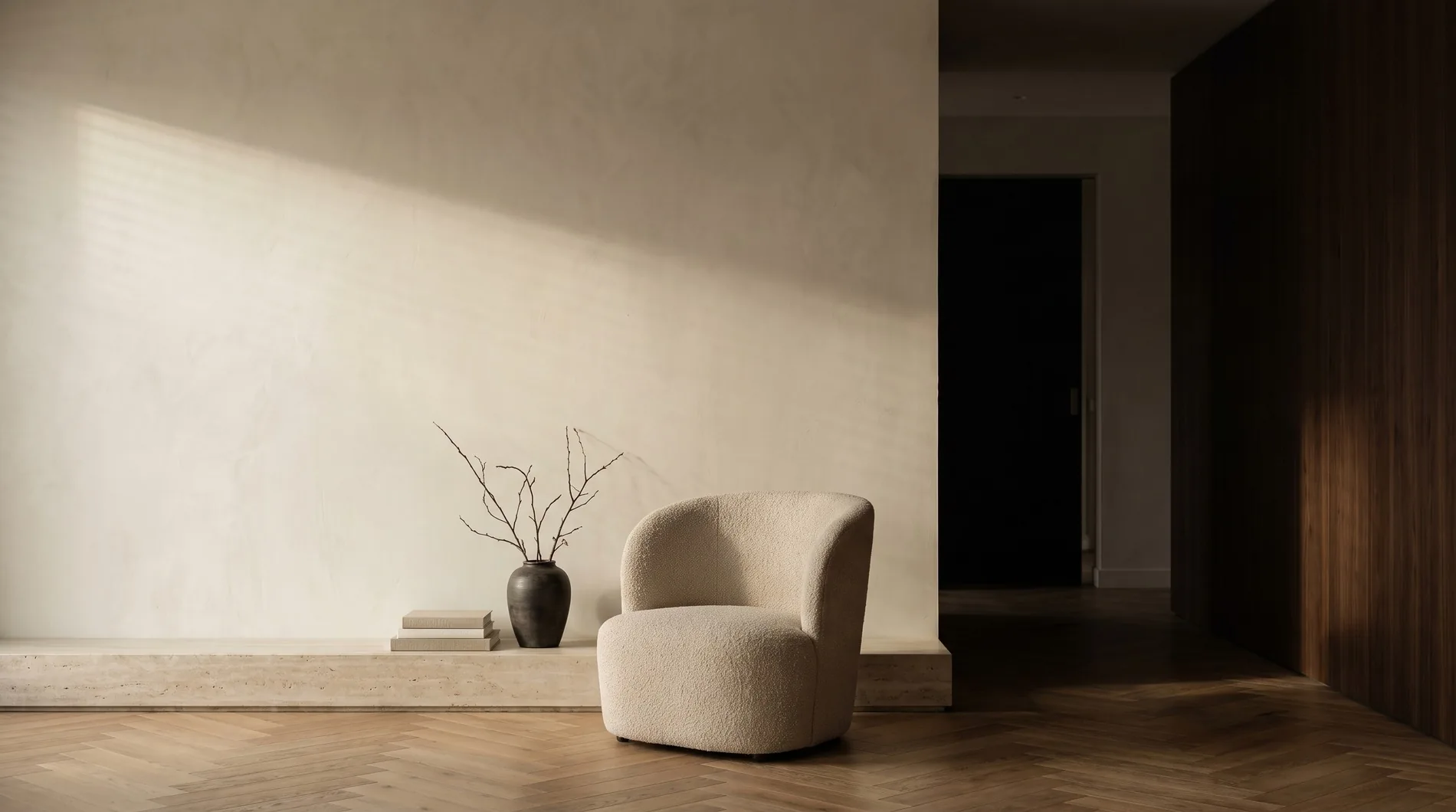 Rustige woonkamer met ochtendlicht op stucwerk, bouclé fauteuil en visgraatparket